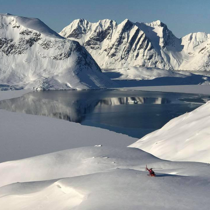 A red Greenland Copter heliskiing helicopter sits quiet surrounded by magnificent glaciers and mountains that make up our heliskiing terrain in Greenland.