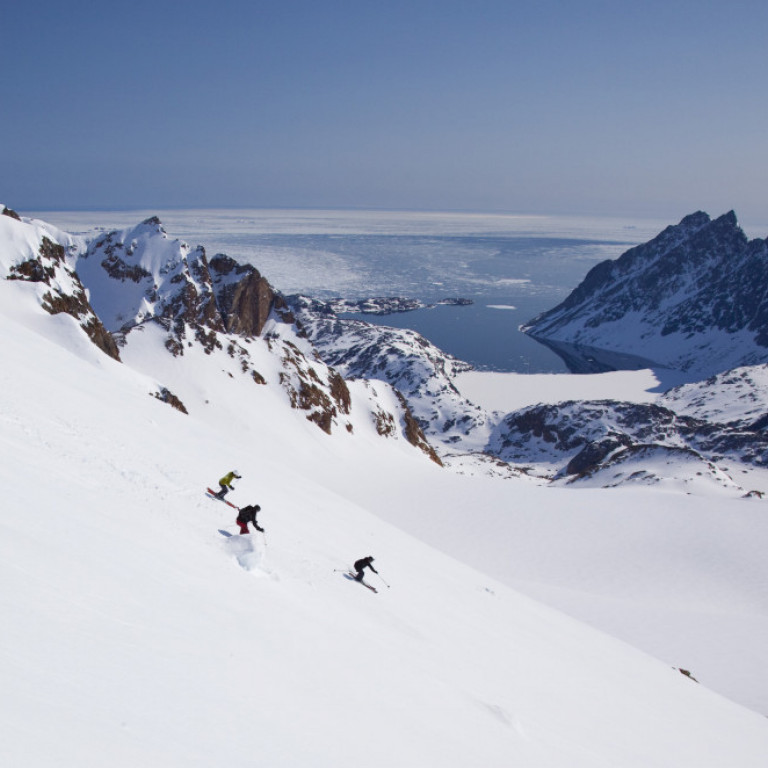 Heli skiers enjoying a beautiful day in Greenland skiing from the summit to the sea shore on great snow in perfect blue bird weather .
