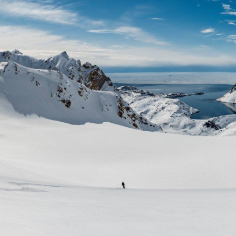 A heli skier looks dwarfed on this massive glacier in Greenland skiing towards the waiting helicopter at the bottom of the run and ready for more heliskiing.