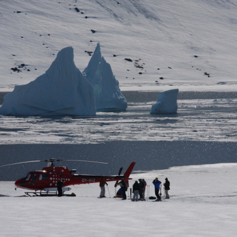 Heli-skiing helicopter picking up a group of skiers next to a giant iceberg on the East Coast of Greenland near Kulusuk in the Ammassalik region.