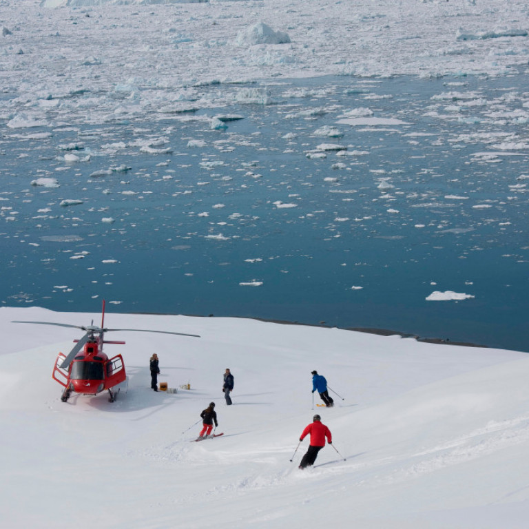 Heli skiers descending towards the helicopter on the waters edge on the East coast of Greenland after another fantastic heli-ski run from summit to sea.
