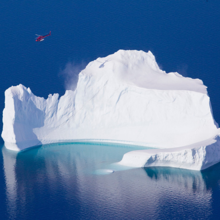 A mammoth of an iceberg dwarfs the red Air Greenland heli-skiing helicopter as it flies over it on the way to another heli ski run in East Greenland.