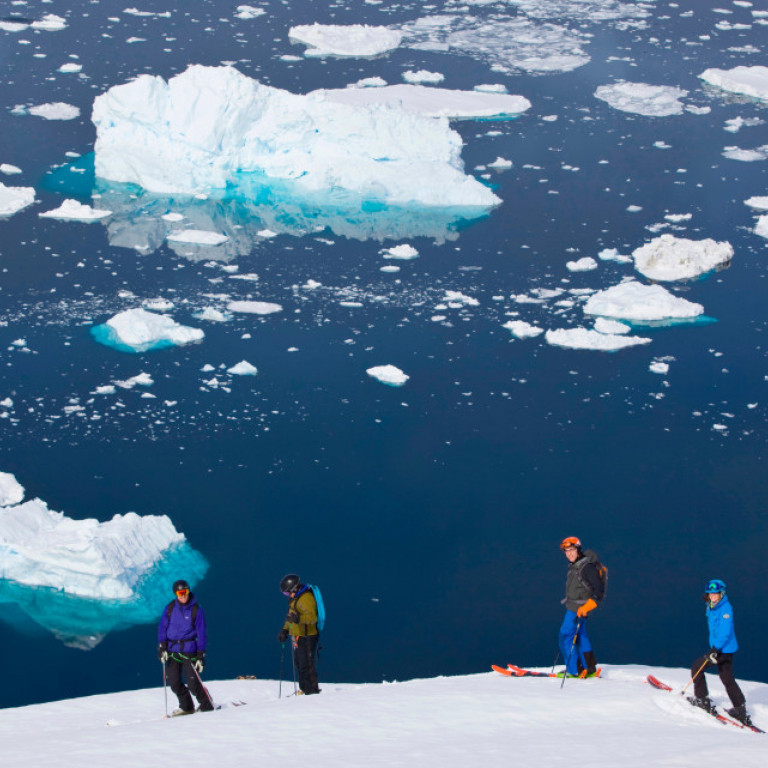 A group of heli skiers takes a moment to pause and take in the breathtaking scenery of East Greenland, one of the world’s greatest heli-skiing places.