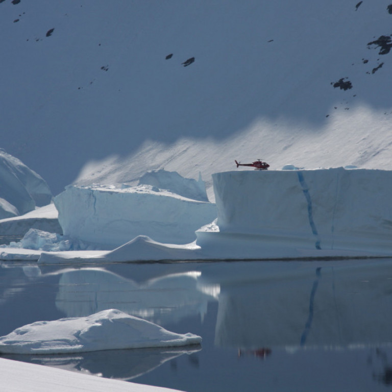 An Air Greenland heliskiing helicopter lands on top of a giant iceberg on the east coast of Greenland before picking up the next group of heli skiers.