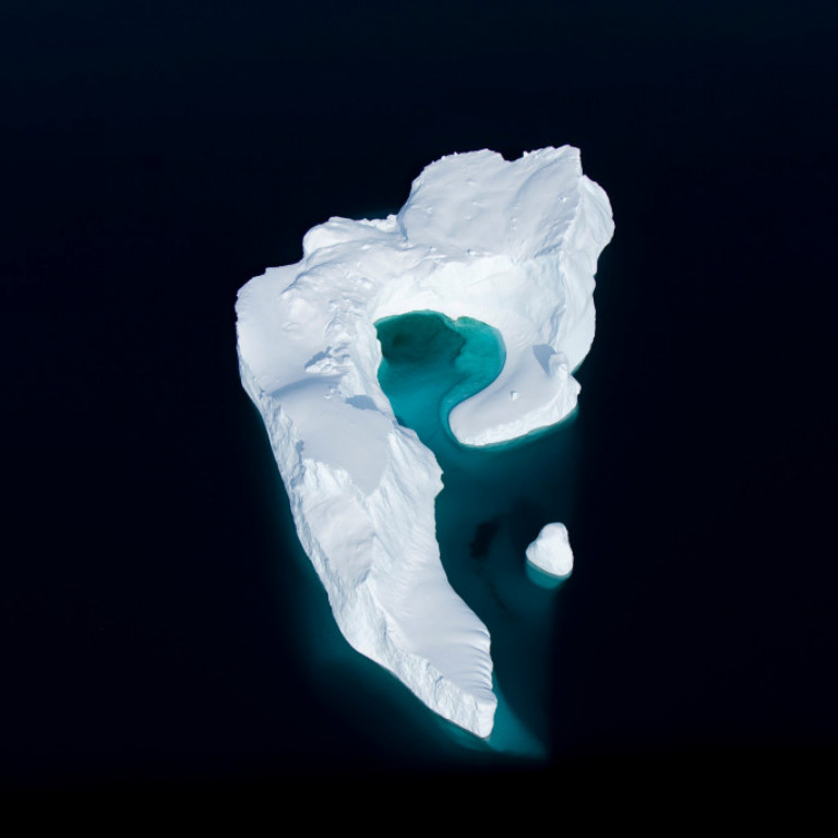 A view from the heli-skiing helicopter over one of many icebergs on the east coast of Greenland. Amazing colors of white on black with a hint of green.