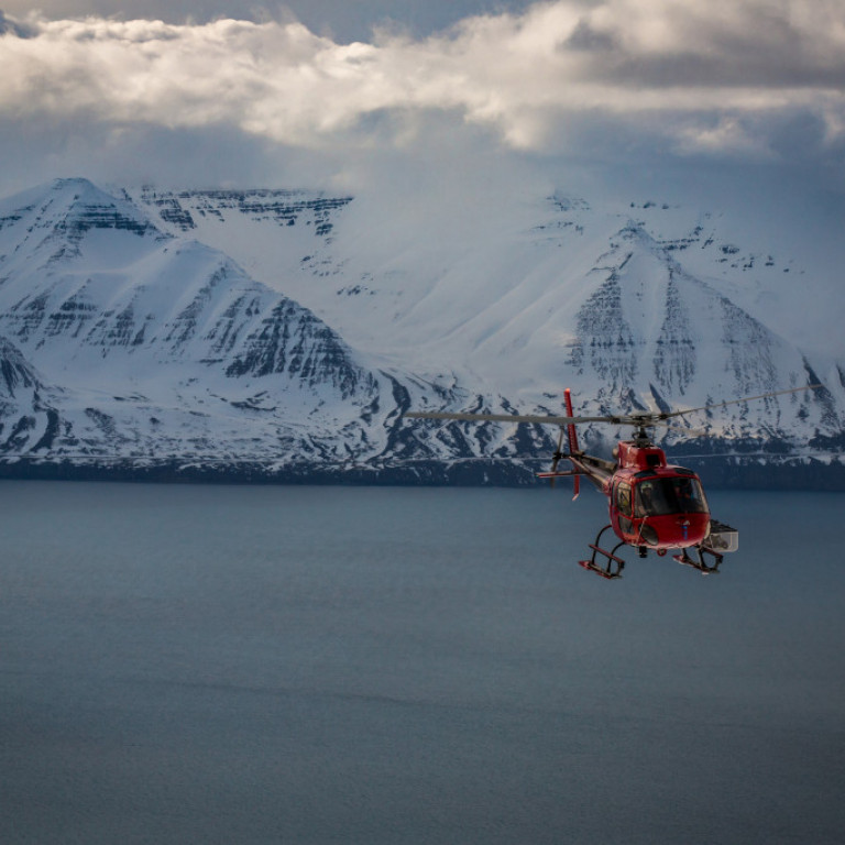 Air Greenland helicopter flying with the mountains of the Troll Peninsula in the background ©Dirk Collins