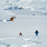 Heliskiers skiing towards the waiting helicopter in Northern Sweden in pristine powder snow conditions and ready for the next heli ski run.